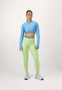 Sinine pikkade varrukatega crop top, millel on lukuga ja must logo bänd; helesinised kõrge vöökohaga legginsid, millel on logo detail. Valged spordijalatsid.