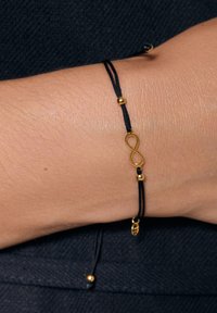 Czarny sznurkowy bracelet z złotym symbolem nieskończoności i dwoma złotymi koralikami. Gładka tekstura z regulowaną długością. Minimalistyczny design.