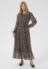 Robe maxi en tissu transparent à motif léopard, avec des manches longues, un col et une jupe à volants. Assortie à des talons noirs.