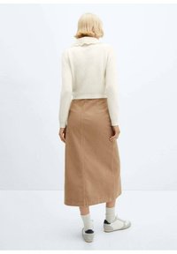 Suéter blanco de punto con cuello festoneado, combinado con una falda larga de pana marrón y zapatillas grises con detalles blancos.