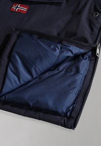 Interno di una giacca navale con una tasca foderata dal design diagonale, texture liscia e una patch del flag norvegese a contrasto all'esterno.