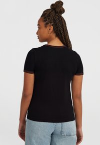 Svart t-shirt med kort ärm och en kontrasterande mörkbrun ribbad krage och ärmslut. Tyget ser mjukt ut och har en figurnära passform.