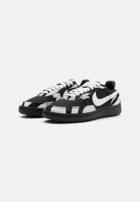 Sneakers bassi realizzati in tessuto e pelle, con un motivo a righe zebrate bianche e nere, dotati di lacci bianchi e una suola in gomma nera.
