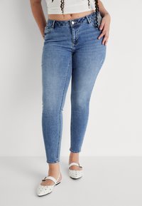 Light blue skinny jeans made of denim, featuring a high waist, front pockets, and a smooth texture. Worn with white shoes adorned with dots.