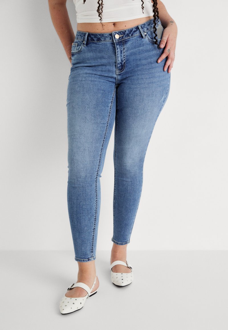 Light blue skinny jeans made of denim, featuring a high waist, front pockets, and a smooth texture. Worn with white shoes adorned with dots.