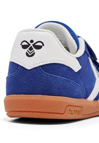 Blå mockaskor med vita detaljer, texturerad gummisula och svart logotext på hälen. Har säker förslutning.