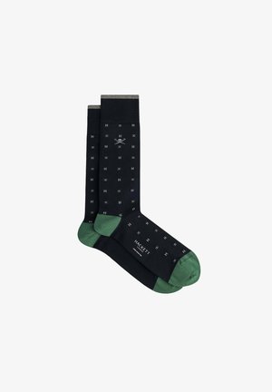 Calcetines negros con acentos verdes, con un patrón de pequeños logotipos blancos de "H" y tijeras cruzadas. Fabricados en un tejido suave con puños en contraste.