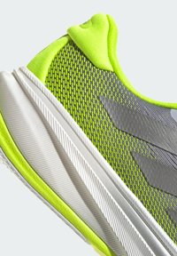 Baskets sportives avec une tige en mesh léger de couleur vert citron et gris, dotées d'une semelle extérieure texturée blanche et d'un relief prononcé pour une meilleure adhérence.