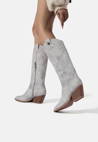Stivali alti in camoscio grigio fino al ginocchio, con cerniera, design perforato e tacco in legno impilato, caratterizzati da cuciture decorative e accenti.