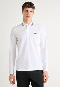 Hvit langermet polo skjorte med ribbet krage som har sorte og fluorescerende gule striper, pyntet med en liten svart "BOSS" logo.