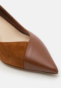 Zapato de punta marrón de cuero y gamuza con un frente liso y paneles texturizados, que presenta un diseño elegante y minimalista.