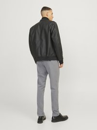 Veste bomber en cuir synthétique noir avec un col à côtes, associée à un pantalon gris ajusté et des chaussures noires à lacets, vue de dos.