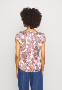 Blusa de manga corta en tejido suave con un estampado de paisley en tonos rosa, amarillo y gris. Cuello redondo con un ojal en la parte posterior.