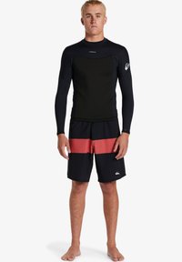 Čierny dlhý rukáv rash guard s textúrovanou látkou, spárovaný s námorníckymi šortkami so červenými horizontálnymi pruhmi a logom.
