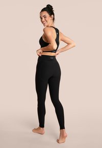 Reggiseno sportivo nero senza cuciture e leggings a vita alta, entrambi realizzati in un tessuto liscio ed elastico, caratterizzati da loghi minimal e un design aderente.