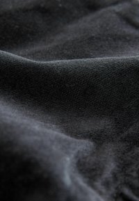 Melna auduma ar mīkstu, teksturētu virsmu, kurā redzamas izplūdušas viļņveida formas un dažādas nokrāsas, radot bagātu dziļumu kopējā izskatā.