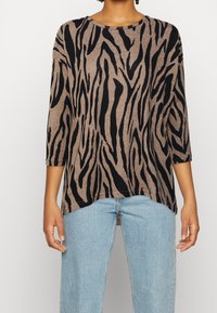 Brun långärmad tröja med svart zebramönster, rund halsringning och lös passform, kombinerad med ljusblå höga jeans.