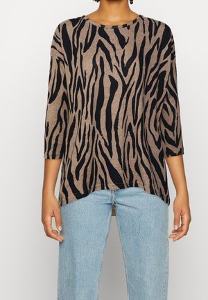 Braunes Langarm-Oberteil mit einem schwarzen Zebra-Streifenmuster, Rundhalsausschnitt und lockerer Passform, kombiniert mit hellblauen hochgeschnittenen Jeans.