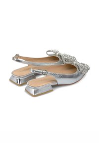 Chaussures slingback argentées avec un accent de nœud texturé, des talons carrés et une finition métallique lisse. L'intérieur présente des semelles en cuir beige.