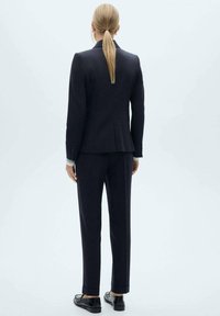 Námořnický oblek na míru s přiléhavým sakem a úzkými kalhotami. Hladká látka s jemnou strukturou, doplněná černými botami.