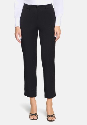 Zwarte op maat gemaakte broek met een gladde textuur, kleine perforaties voor detail, en een verkorte lengte, gecombineerd met zwarte sandalen met bandjes.