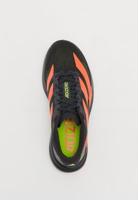 Black athletic shoe with orange stripes. Features a breathable mesh upper, green insole, and smooth black sole with textured accents.