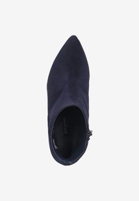Botines de ante azul marino con punta afilada, cremallera lateral y textura suave. El interior cuenta con una plantilla con marca y un diseño minimalista.
