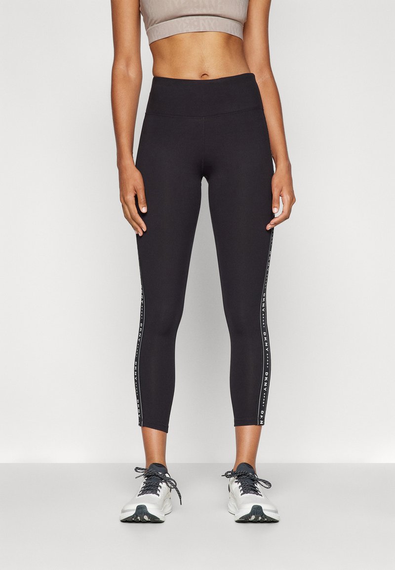 Svarte, korte leggins laget av elastisk stoff, med høy midje og kontrastfargede sidestriper med "DKNY"-tekst.