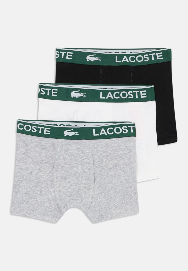 Trīs Lacoste boxer apakšveļas komplekti: pelēki, balti un melni. Katram ir zaļa elastīga josta ar baltu zīmolu un logo.
