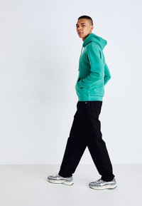 Teal hooded sweatshirt with front pocket, black pants, and multicolored athletic shoes. Simple design and relaxed fit.