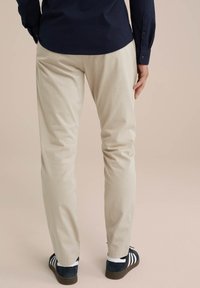 Pantaloni bej din material de bumbac, cu un design drept. Purtați cu adidași cu dungi negre și albe. Detalii vizibile de cusătură.