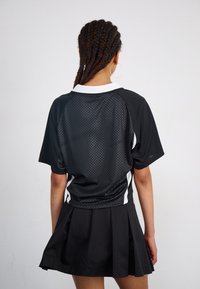 Top atletico nero con texture a rete e accenti bianchi, abbinato a una gonna plissettata nera. Presenta un colletto e maniche corte.