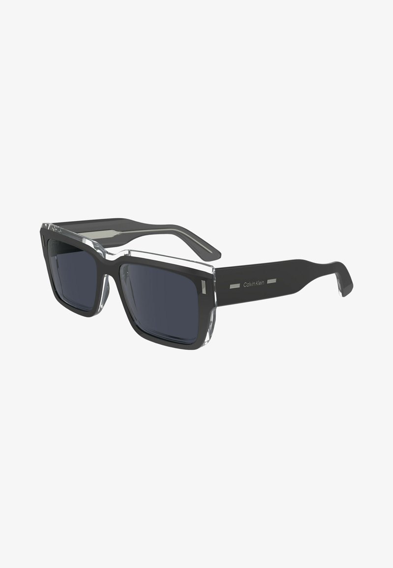 Black rectangular sunglasses with dark gray lenses, featuring a transparent frame tip and a sleek solid black arm. "Calvin Klein" logo on arm.
