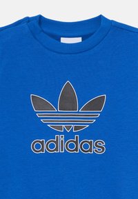 Modra bombažna pulover s kratkimi rokavi z velikim sivim logotipom Adidas trefoil in besedilom. Gladka tekstura z rebrastim ovratnikom.