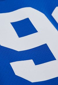 Gros plan sur le numéro 23 blanc brodé sur un tissu en maille sportive respirante bleu.