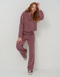 Rot gestreifte cordjacke und weit geschnittene hose mit aufgesetzten taschen und knopfverschluss. Getragen mit grauen sneakers, vor einem schlichten hintergrund.