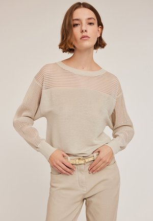 Maglione leggero beige con strisce orizzontali trasparenti. Presenta maniche lunghe e un colletto rotondo, abbinato a pantaloni chiari e una cintura.