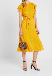 Gul klänning med prickmönster, volangärmar, midjeband och utsvängd fåll. Matchad med en leopardmönstrad handväska och svarta remsandaler.