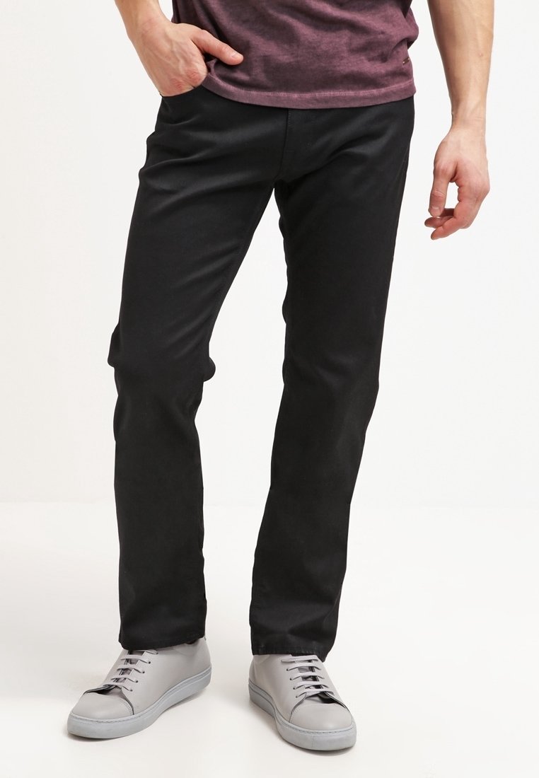 Pantalones negros de corte ajustado y tela suave, combinados con zapatillas deportivas grises. Los pantalones tienen un diseño clásico y corte recto en la pierna.