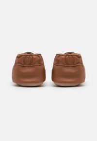 Pantofi de bebeluși din piele maro, cu deschideri elastice, tălpi moi și un design strâns la spate, creând o fixare confortabilă.