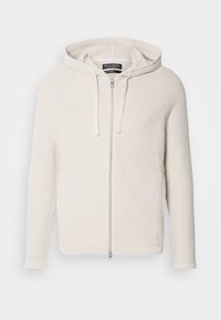 Lys beige zip-opp hettejakke med et teksturert strikkedesign, har stropp foran og ribbet mansjetter. Subtil logoakkent nær sømmen.