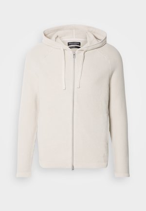 Light beige zip-up hoodie with a textured knit design, featuring a drawstring hood and ribbed cuffs. Subtle logo accent near the hem.