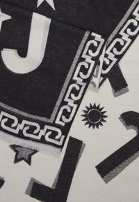 Tissu noir et blanc avec de grandes lettres, des symboles de soleil et d'étoile, ainsi qu'un motif de bordure en chaîne décorative, plié montrant les deux côtés.