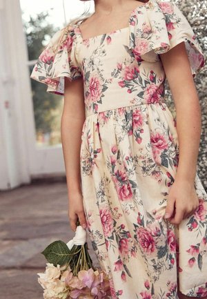 Robe fleurie avec un décolleté carré et des manches volantées, fabriquée en tissu léger aux couleurs pastel. Le modèle tient un bouquet de fleurs.