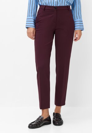 Donna che indossa pantaloni bordeaux a gamba dritta, una camicia blu a righe con ampi polsini e mocassini neri in pelle.