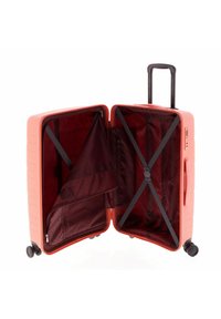 Harde koffer in koraal met zwarte wielen. Het interieur bevat bordeauxrode stof, inpakriemen en een ritsvak.