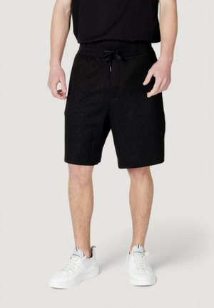 Shorts neri con un motivo a diamante testurizzato, dotati di un elastico in vita con stringa. Abbinati a scarpe da ginnastica bianche e a una maglietta nera.