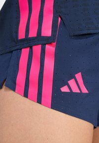 Granatowe szorty wykonane z lekkiego materiału, z różowymi paskami i perforacjami, z odblaskowym logo Adidas z boku.