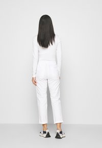 Camisa blanca de manga larga y pantalones blancos, con corte recto. Zapatillas negras y beiges con suela texturizada. Diseño simple y minimalista.