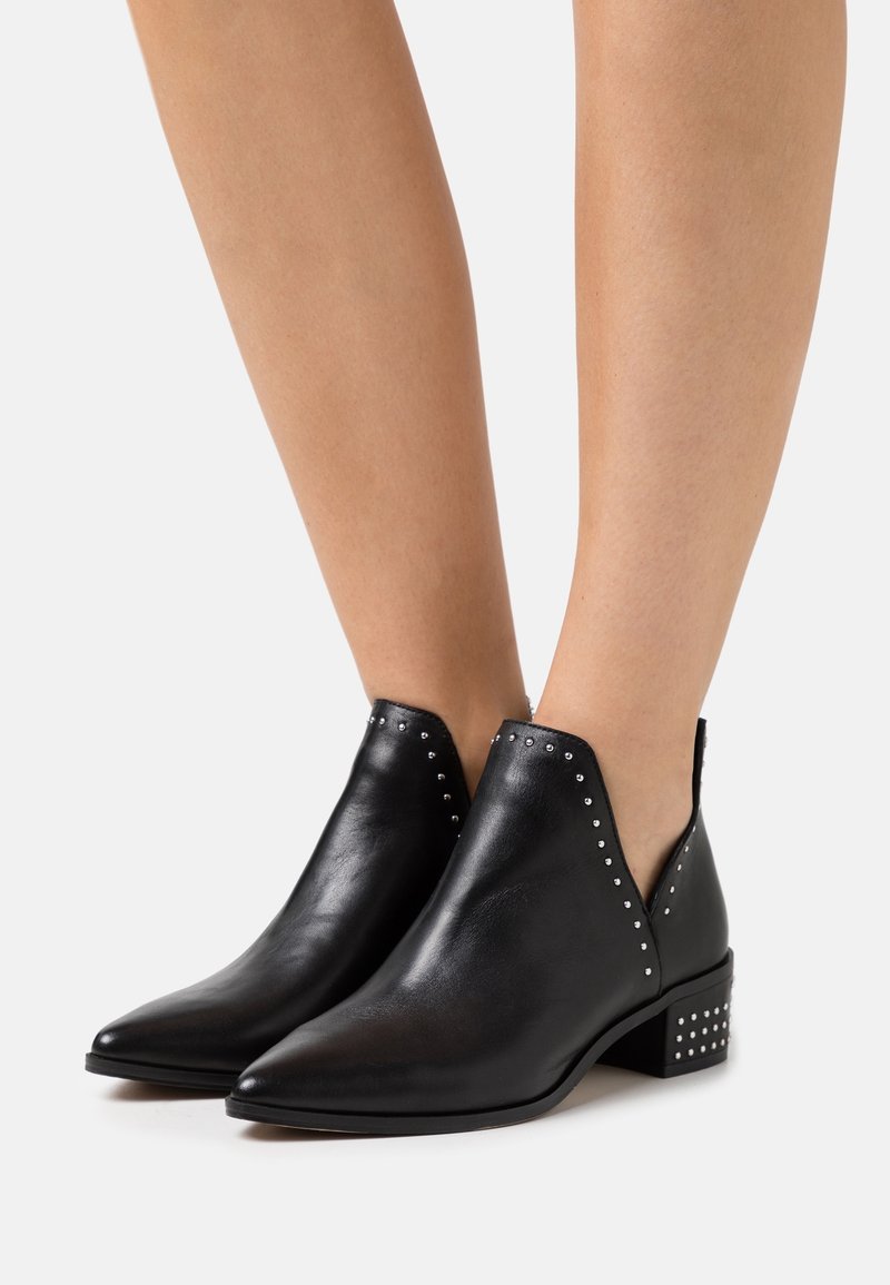 Bottines en cuir noir avec un bout pointu, des côtés découpés, des accents en clous argentés et un petit talon block. Texture lisse.